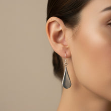 Load image into Gallery viewer, A pair of silver teardrop-shaped dangle earrings with fishhook wires, displayed on a textured teal background.