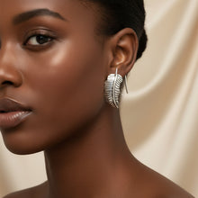 Load image into Gallery viewer, A pair of silver-toned metal earrings shaped like stylized feathers, displayed on a light background.
