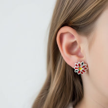 Charger l'image dans la galerie, A pair of silver-toned flower-shaped earrings with red and green enamel petals and a yellow centre, shown on a clear background.
