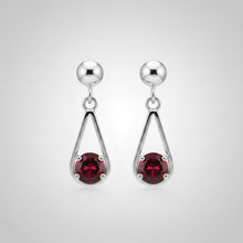 Load image into Gallery viewer, Silver dangle earrings with a teardrop-shaped design, featuring a polished silver post and a drop composed of a red faceted crystal and a silver disc with a red band, displayed on a textured light blue and white surface.
